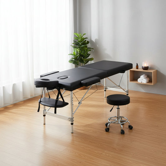 Black massage table with adjustable silver metal frame shown open, alongside a matching black rolling stool on a white background.